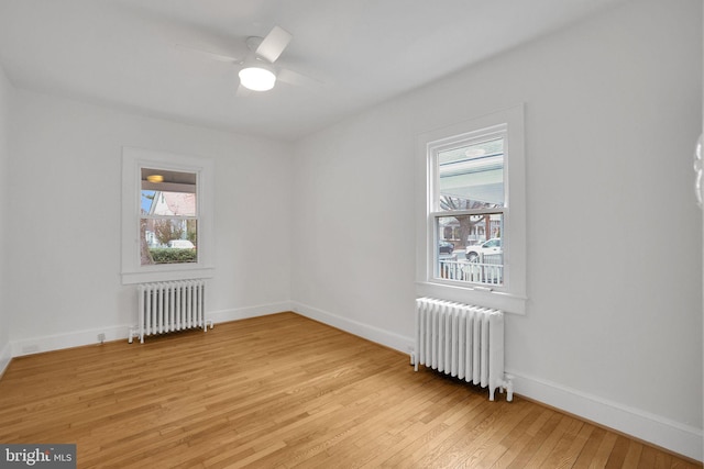 spare room with baseboards, light wood finished floors, a ceiling fan, and radiator