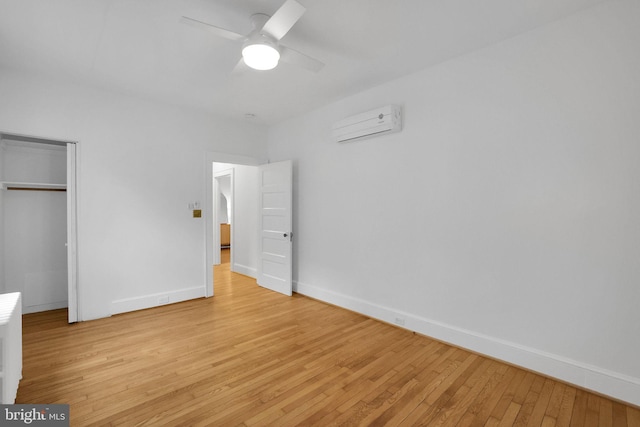 unfurnished bedroom featuring a wall unit AC, light wood-style flooring, a ceiling fan, baseboards, and a closet