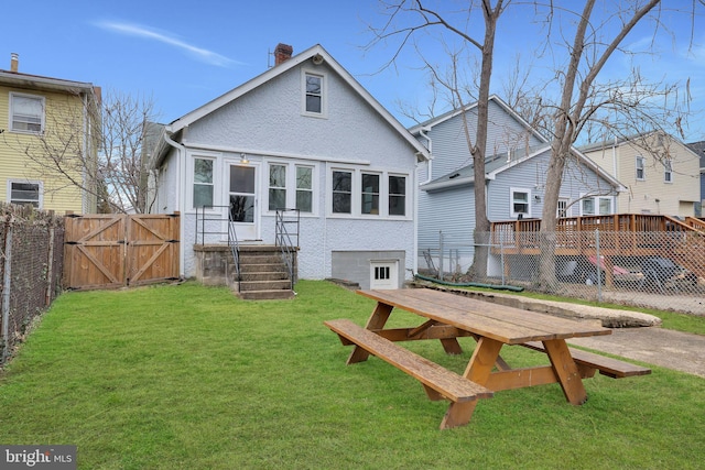 rear view of house featuring a yard, a chimney, fence, and a gate