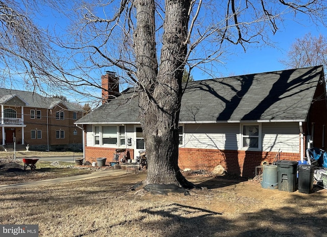 back of property featuring a shingled roof, a chimney, and brick siding