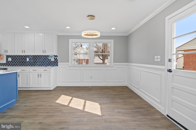 kitchen with light countertops, ornamental molding, wood finished floors, and white cabinetry