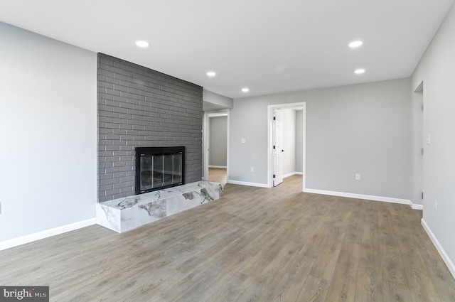 unfurnished living room with a brick fireplace, baseboards, and wood finished floors