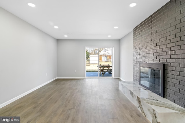 unfurnished living room with a brick fireplace, baseboards, wood finished floors, and recessed lighting