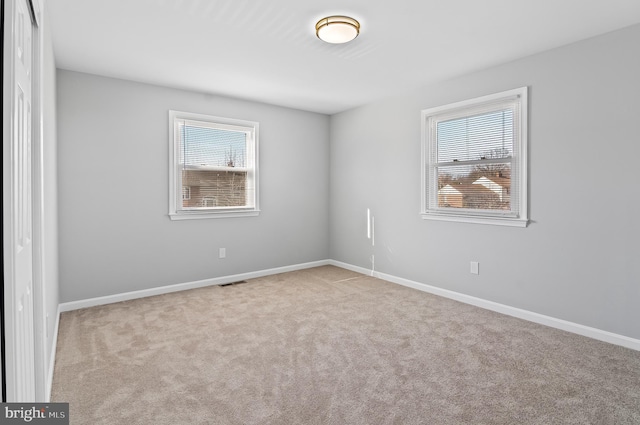 carpeted spare room with visible vents, a wealth of natural light, and baseboards