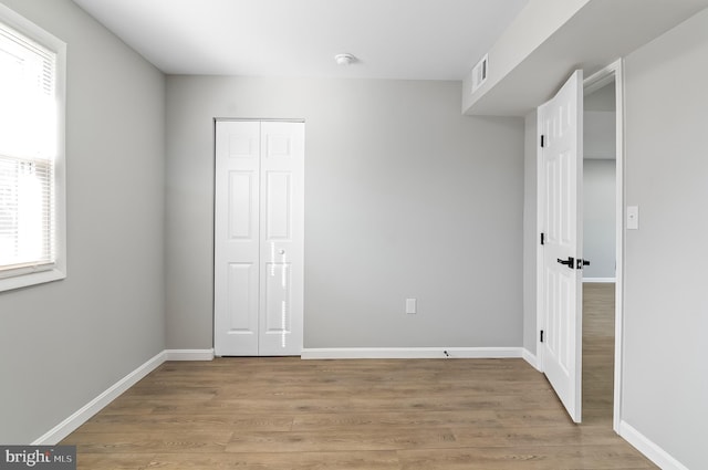 unfurnished bedroom featuring light wood finished floors, baseboards, visible vents, and a closet