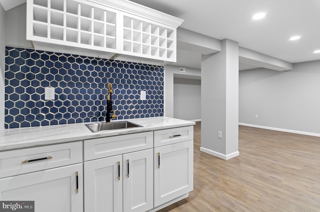 kitchen with baseboards, decorative backsplash, light wood-style flooring, white cabinetry, and a sink