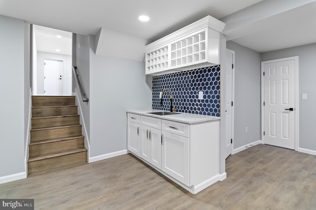 kitchen featuring light countertops, white cabinetry, a sink, light wood-type flooring, and baseboards