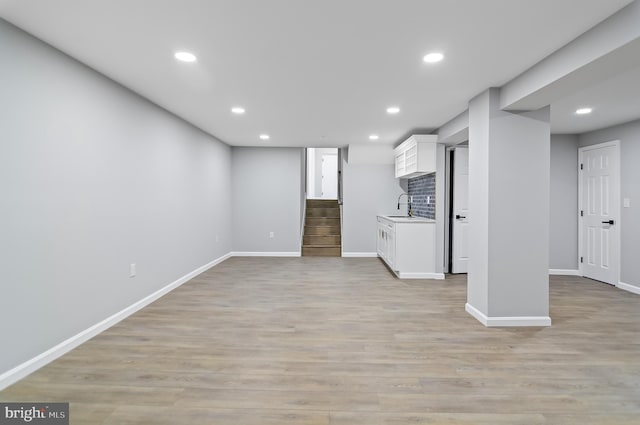 unfurnished living room with light wood-type flooring, stairs, a sink, and recessed lighting