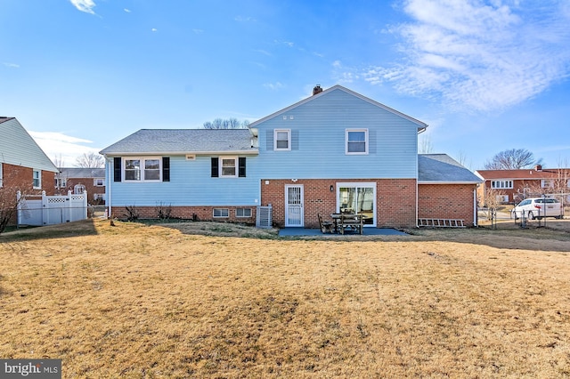 rear view of house with a yard, brick siding, a patio, and fence