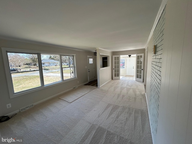 carpeted empty room with visible vents, french doors, baseboards, and ornamental molding