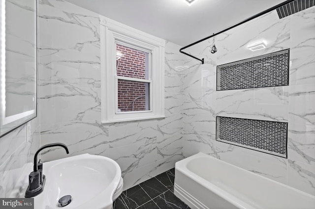 full bath with marble finish floor, stone wall, bathtub / shower combination, and a sink