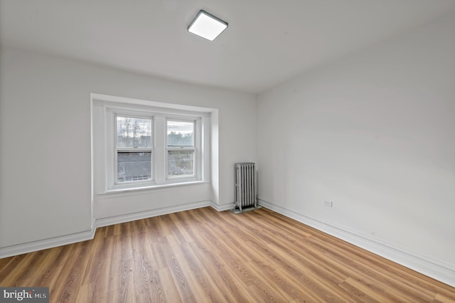 empty room with baseboards, light wood finished floors, and radiator heating unit