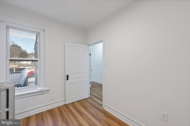 unfurnished room with baseboards, radiator heating unit, and wood finished floors