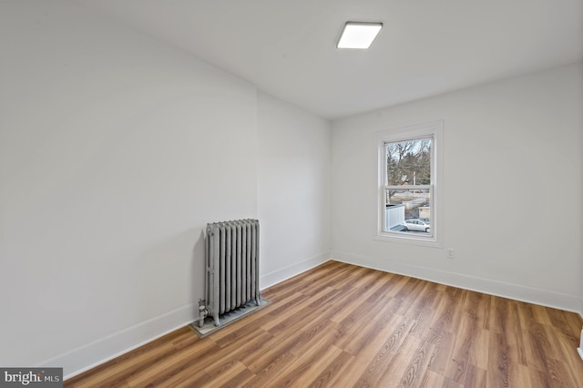 unfurnished room with baseboards, radiator heating unit, and wood finished floors