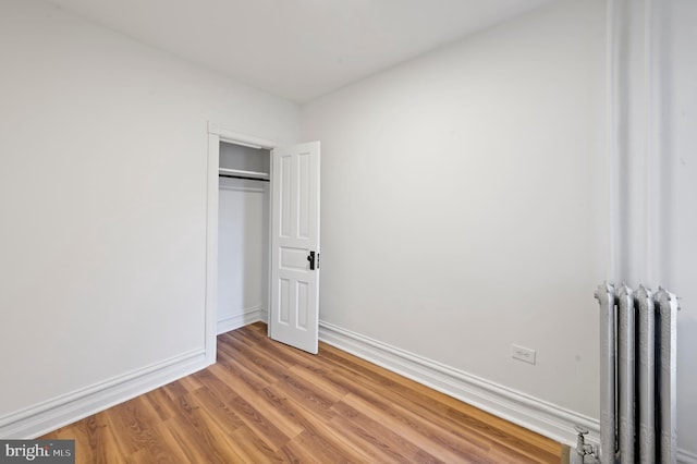 unfurnished bedroom with light wood-style floors, a closet, baseboards, and radiator heating unit