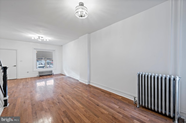 interior space with wood-type flooring, baseboards, radiator heating unit, and an inviting chandelier