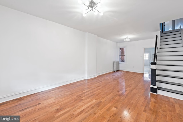 unfurnished living room featuring light wood-style flooring, baseboards, stairway, and radiator heating unit