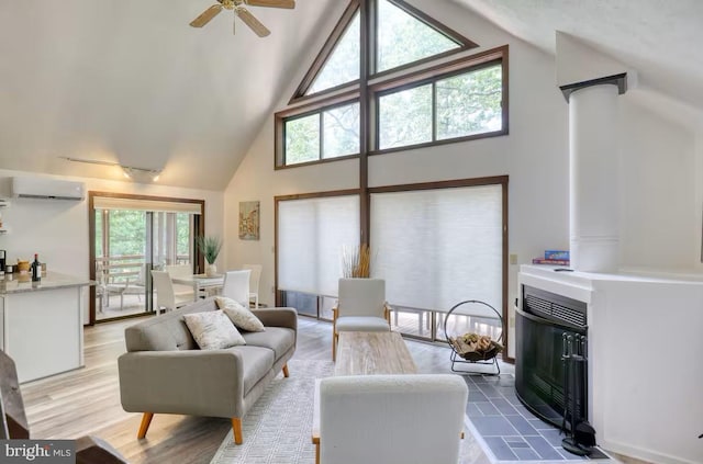 living room with ceiling fan, high vaulted ceiling, light wood-style floors, a wall mounted air conditioner, and a glass covered fireplace