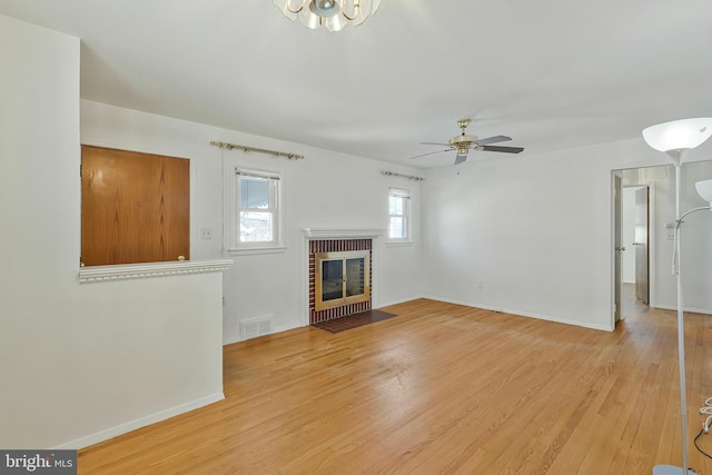 unfurnished living room with light wood finished floors, a brick fireplace, visible vents, and baseboards