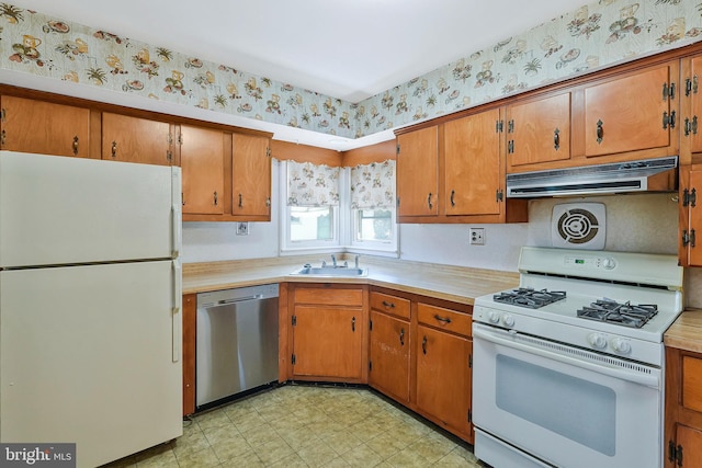 kitchen with white appliances, wallpapered walls, light countertops, under cabinet range hood, and a sink