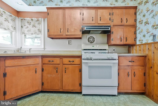 kitchen with under cabinet range hood, white gas range oven, light countertops, and wallpapered walls