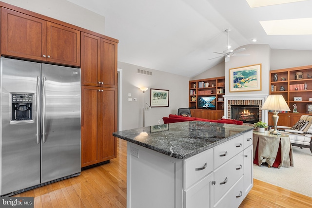 kitchen with stainless steel fridge with ice dispenser, light wood finished floors, a fireplace, lofted ceiling, and dark stone counters