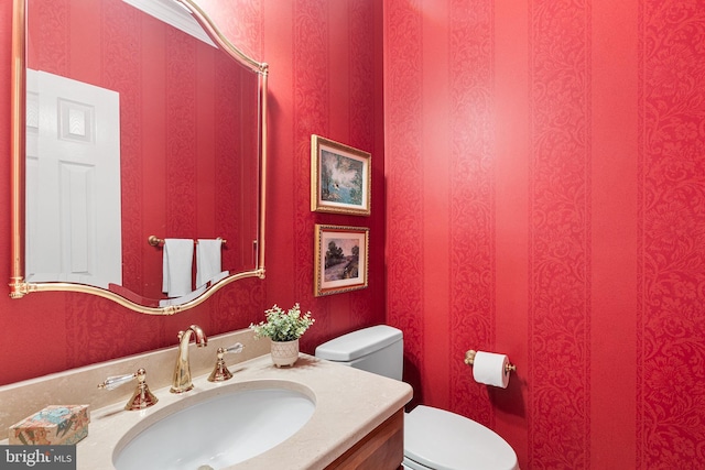 bathroom featuring toilet, vanity, and wallpapered walls