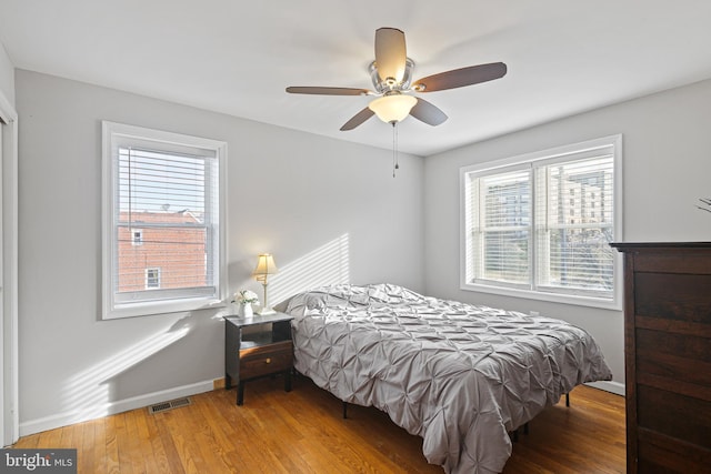 bedroom featuring a ceiling fan, wood finished floors, visible vents, and baseboards