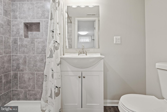 bathroom with vanity, toilet, baseboards, and tiled shower