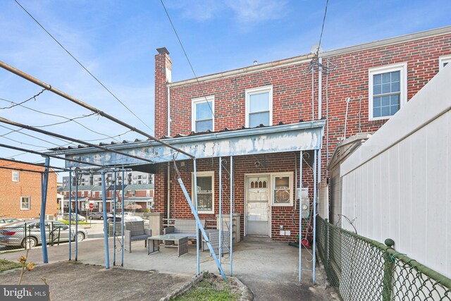 back of property featuring brick siding, covered porch, a chimney, and fence