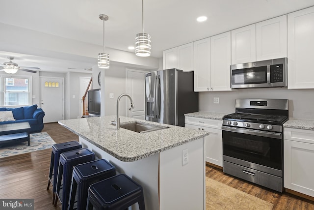 kitchen with open floor plan, a breakfast bar area, appliances with stainless steel finishes, white cabinetry, and a sink