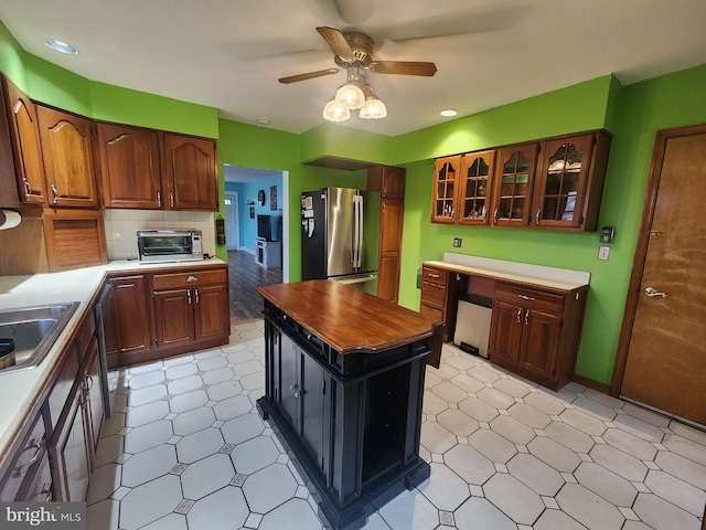 kitchen with built in study area, glass insert cabinets, freestanding refrigerator, light countertops, and light floors