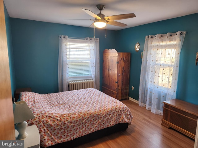 bedroom with radiator heating unit, baseboards, ceiling fan, and wood finished floors