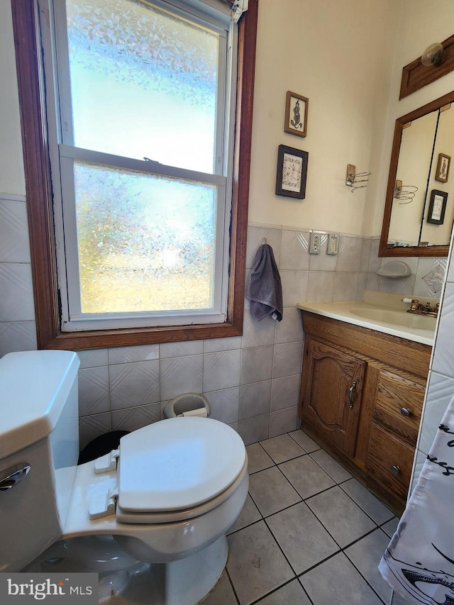 half bathroom featuring a wainscoted wall, tile walls, toilet, vanity, and tile patterned flooring