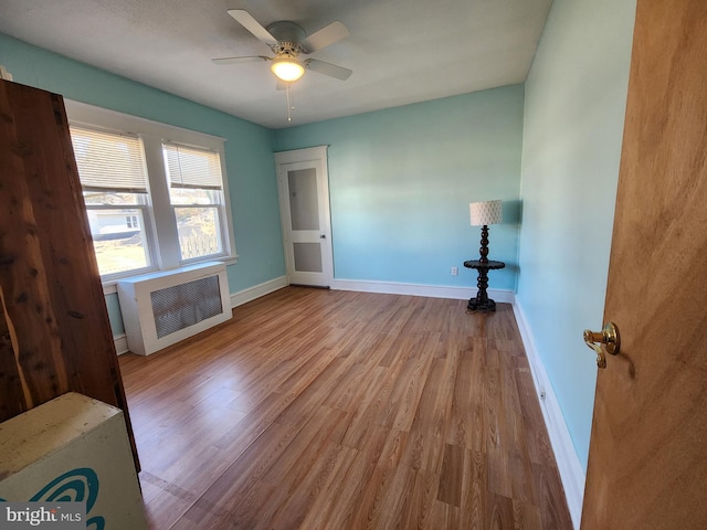 unfurnished room with radiator, ceiling fan, baseboards, and wood finished floors