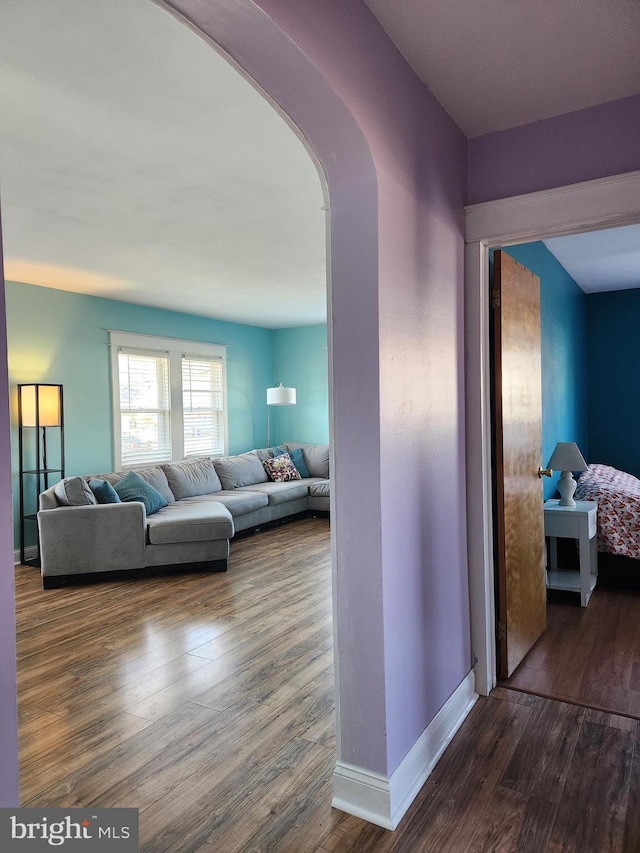 corridor featuring baseboards, arched walkways, and dark wood-type flooring