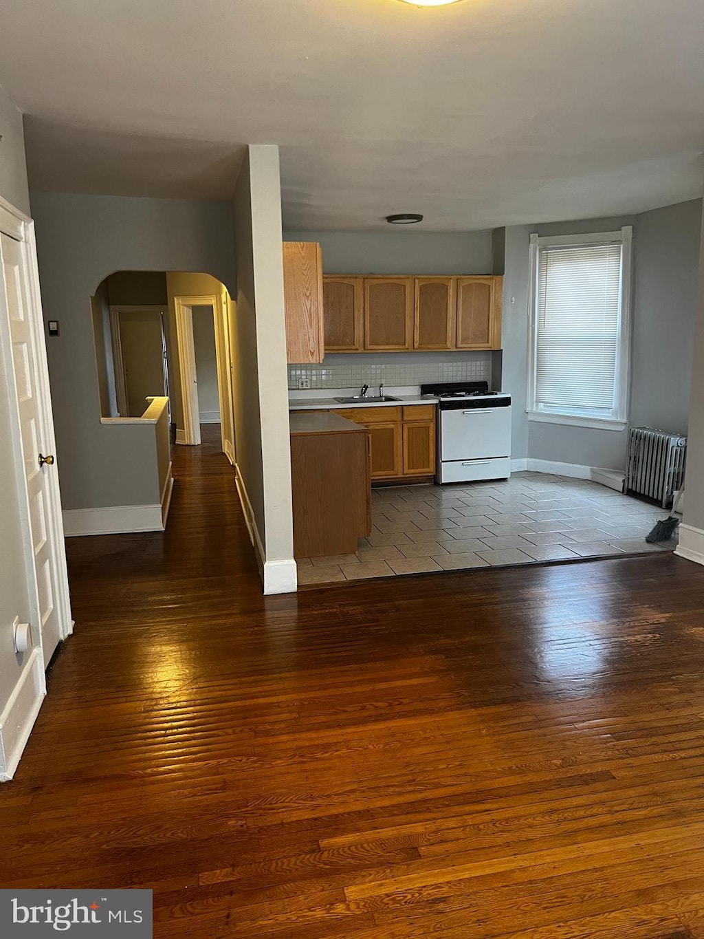 kitchen with radiator, dark wood-type flooring, white gas stove, decorative backsplash, and arched walkways