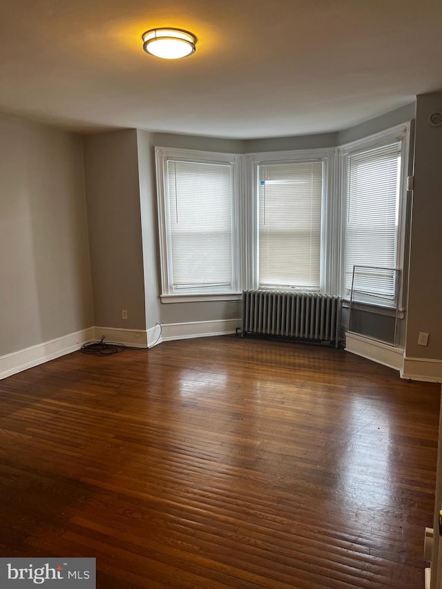 unfurnished room featuring radiator, dark wood-style floors, and baseboards