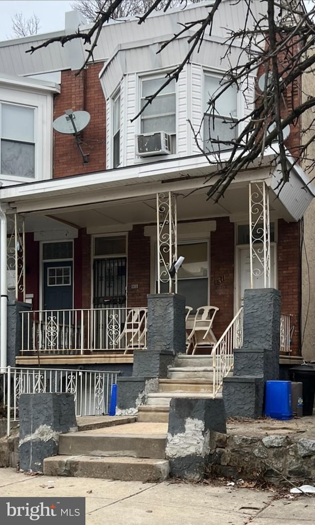 entrance to property featuring cooling unit, brick siding, and covered porch