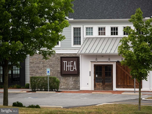 view of front of house featuring stone siding, metal roof, roof with shingles, a standing seam roof, and french doors