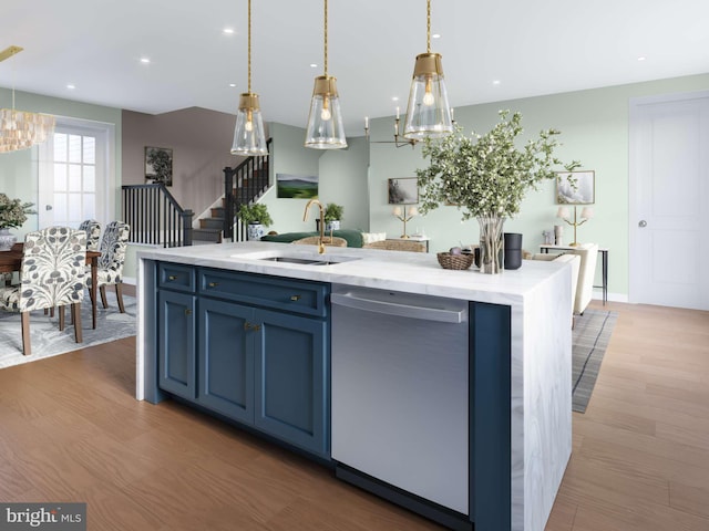 kitchen with light wood finished floors, a center island with sink, blue cabinetry, pendant lighting, and stainless steel dishwasher