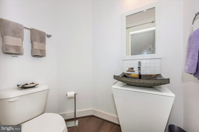 bathroom with wood finished floors, baseboards, a sink, toilet, and tasteful backsplash