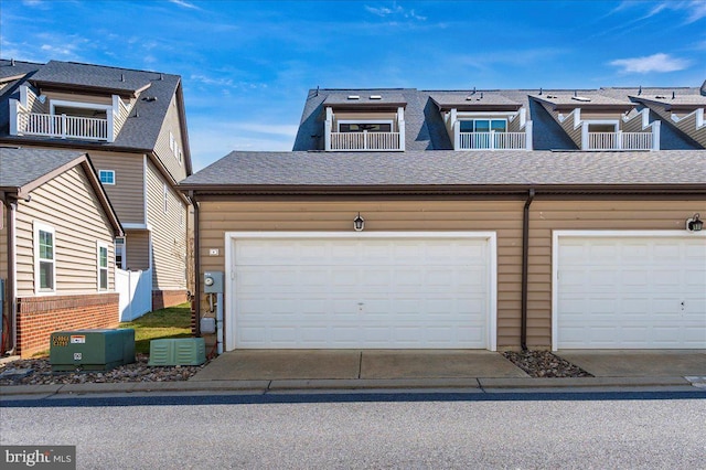 view of property with concrete driveway, a balcony, a garage, and roof with shingles