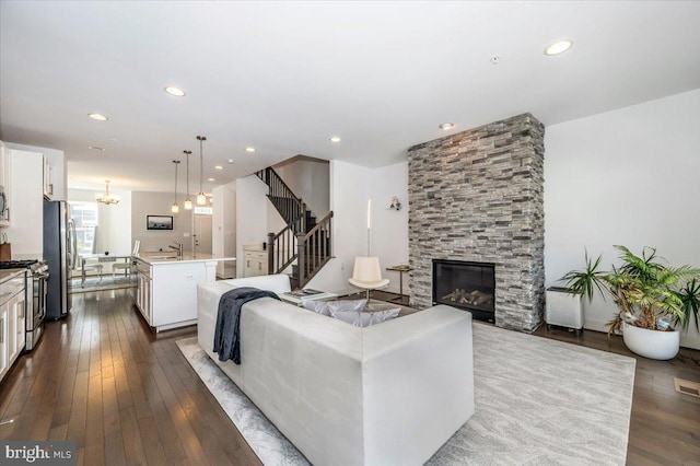 living room with stairs, recessed lighting, a fireplace, a notable chandelier, and dark wood-style flooring