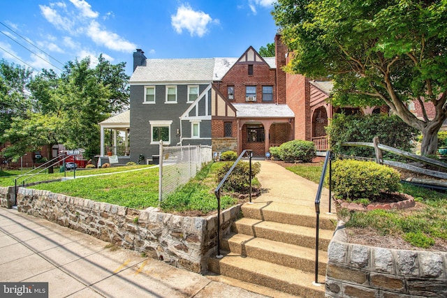 tudor-style house with brick siding, fence, a chimney, and a front lawn