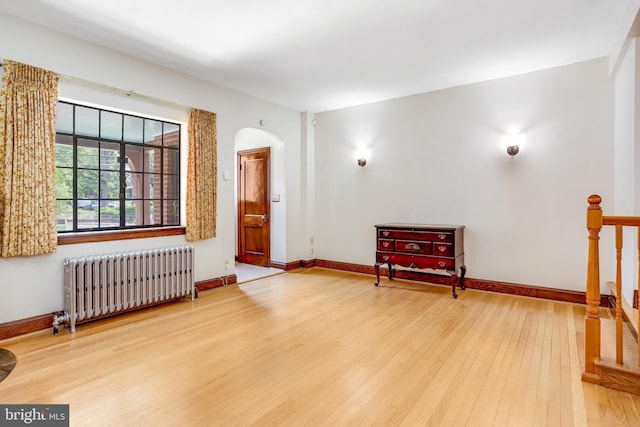 living area featuring arched walkways, baseboards, hardwood / wood-style floors, and radiator heating unit