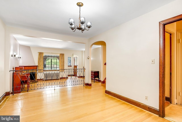 unfurnished room with arched walkways, wood finished floors, baseboards, radiator heating unit, and an inviting chandelier