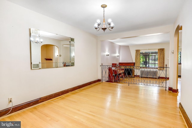 empty room with a chandelier, radiator heating unit, wood finished floors, and baseboards