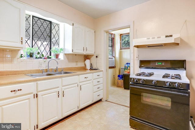 kitchen featuring white cabinets, gas range, backsplash, under cabinet range hood, and a sink