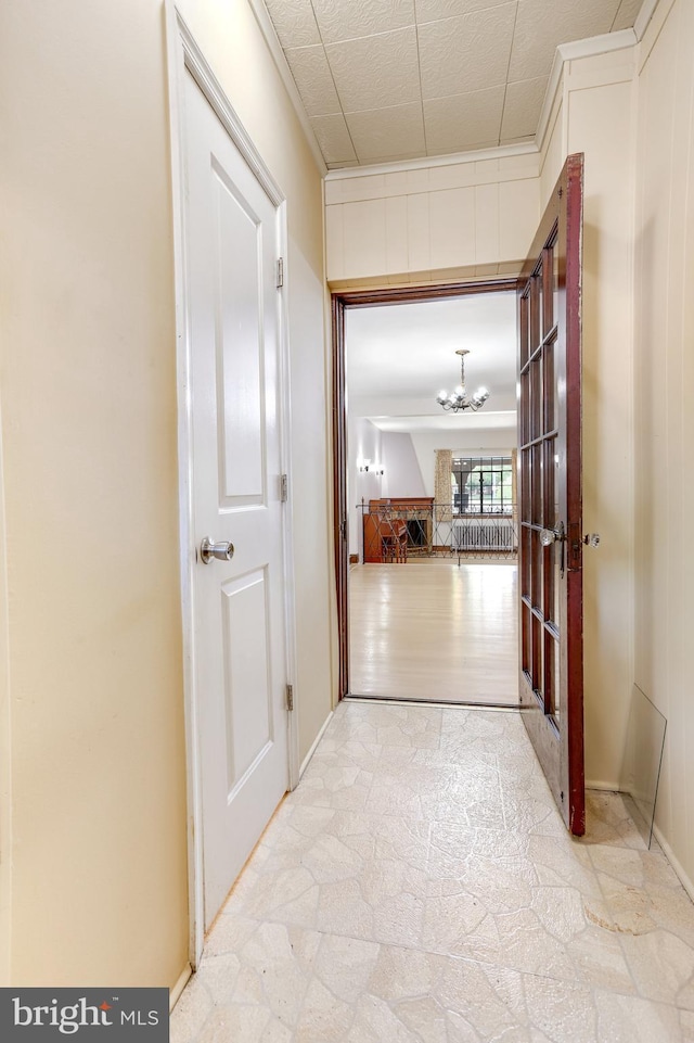 corridor featuring baseboards, stone finish floor, and a notable chandelier